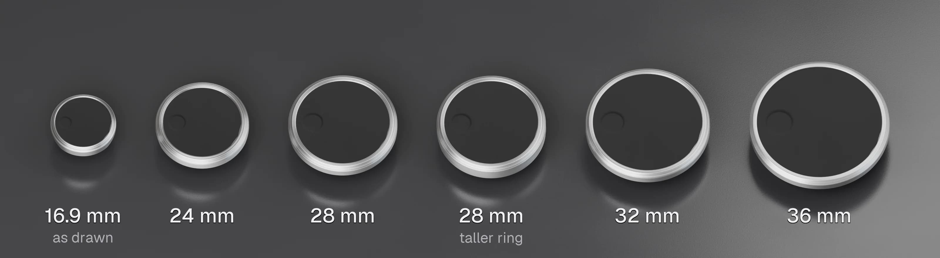 Six test pucks in a row at true scale on a semi-gloss black surface, each a brushed aluminium ring around a dark matte face with its finger dimple: 16.9 mm as drawn, then 24, 28, 28 with a taller ring, 32 and 36 mm, each labelled.